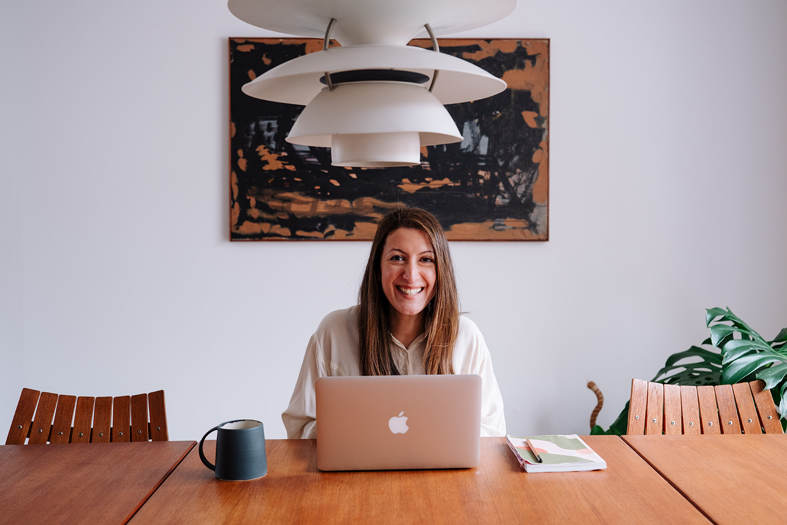 Smiling broadly at the camera from behind an open laptop at a wooden table.