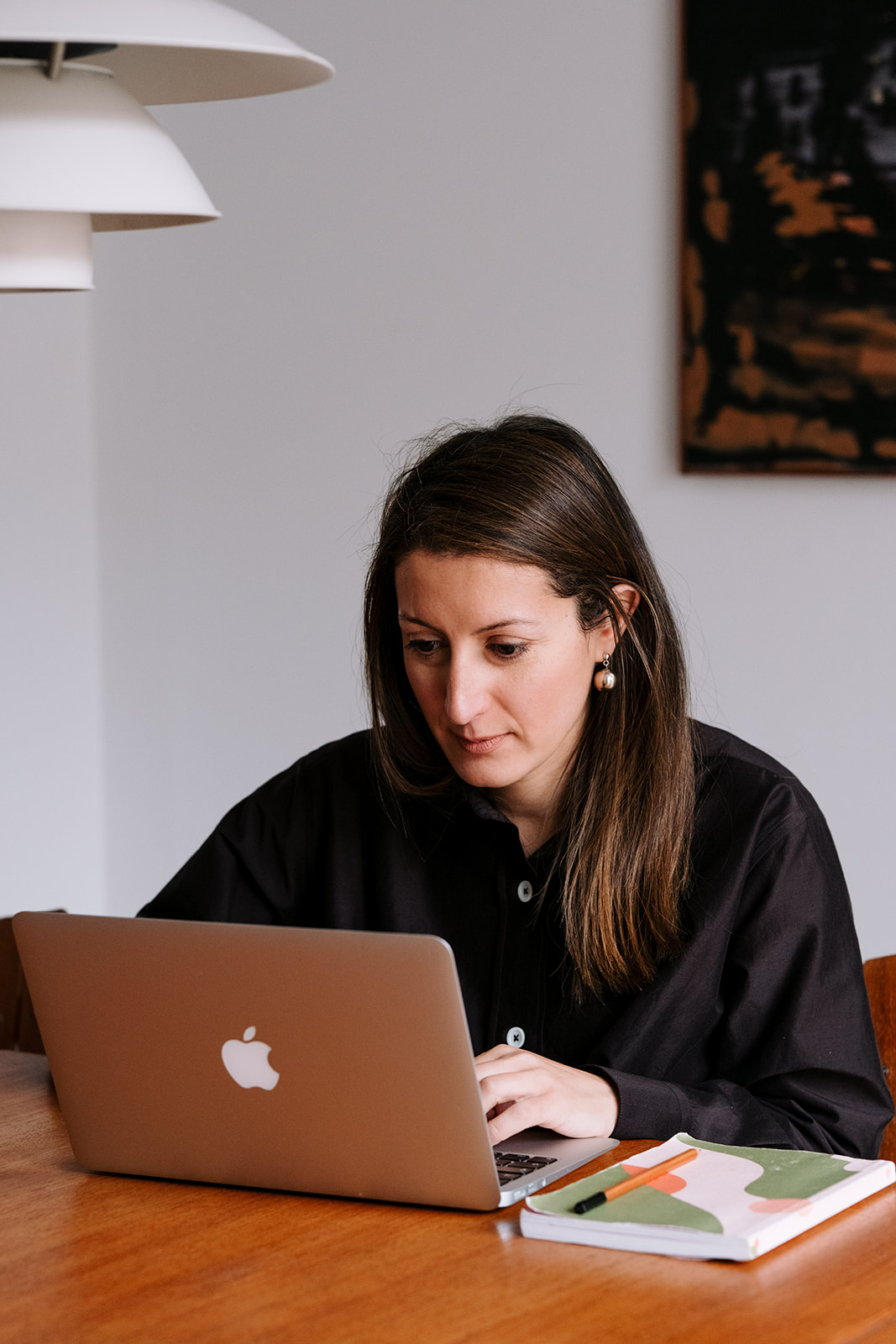 Working at a laptop, concentrating on the screen, with a notebook beside her.