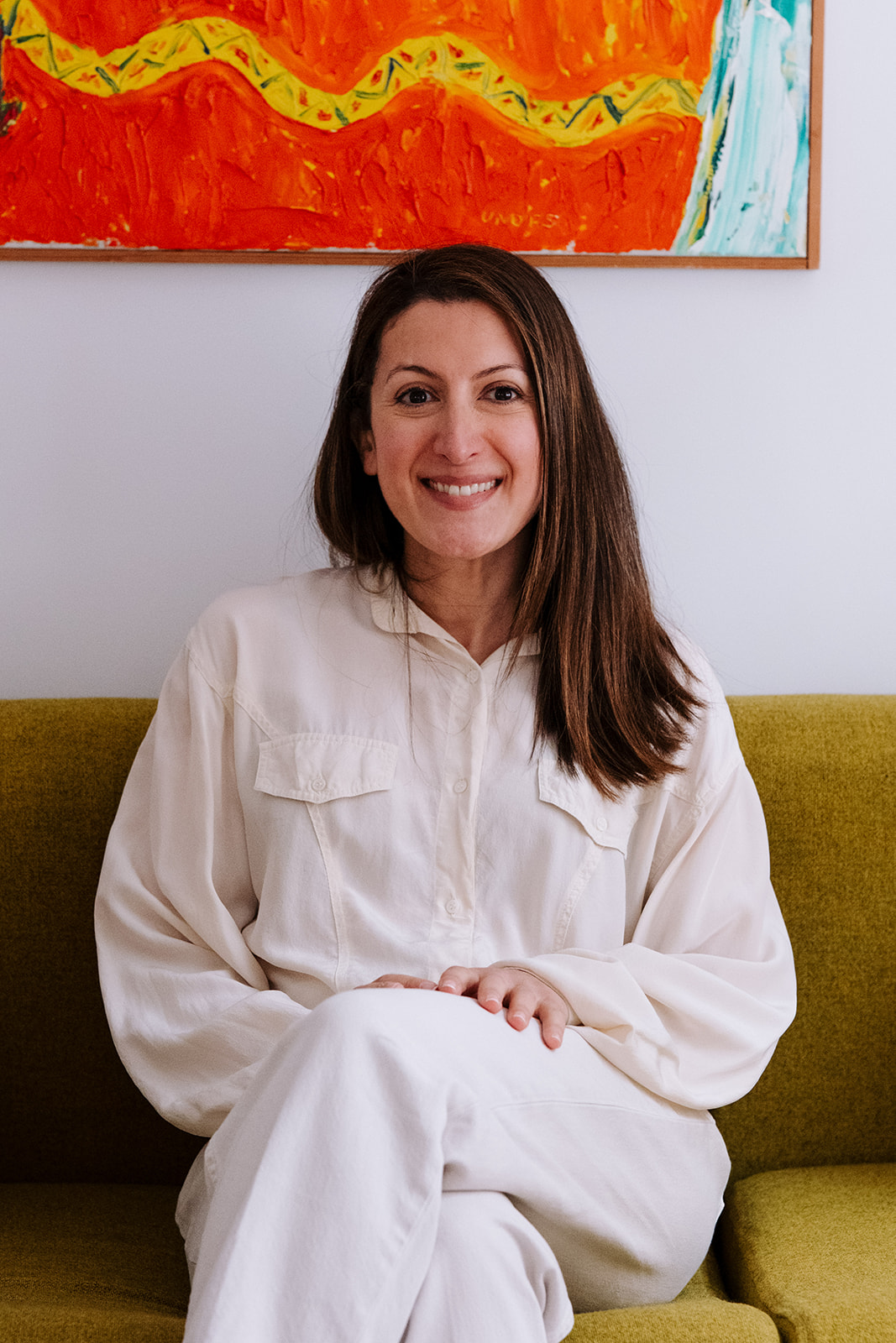 Sitting on a sofa, smiling openly at the camera.